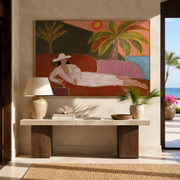 Coral Sunset Lengthens the Lounge - Reclining Woman beneath Palms painting by Claire Whitmore, modern coastal horizontal wall art – styled room scene view 1