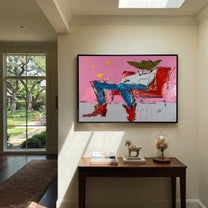 Red Chair Drifts Pink - reclining cowboy chair painting by Ethan Mercer, contemporary Western horizontal wall art – styled room scene view 1